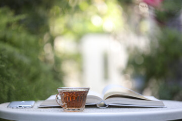 Transparent tea cup with open book and phone on white desk

