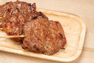 Thai grilled pork in a wooden plate on wooden table.