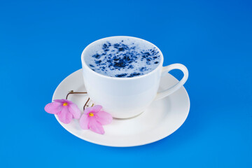 Cup of blue matcha latte with pink flowers on a blue background.