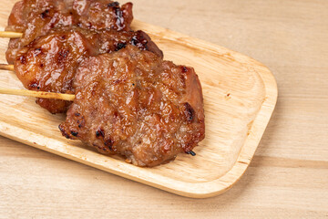 Thai grilled pork in a wooden plate on wooden table.