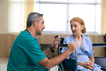 Fototapeta premium Middle age surgeon talking and consultant to senior woman patient in wheelchair. Senior woman on wheelchair and her young caregiver talk care at each other.