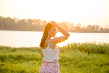 Gentle silhouette of a girl in the rays of the setting sun on the river bank.