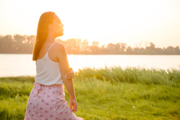 Gentle silhouette of a girl in the rays of the setting sun on the river bank.