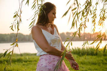 A pensive girl lost in her thoughts, at sunset, among willow leaves. Portrait of a pensive girl on the bank of the river, in the willow foliage.