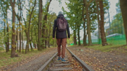 Fototapeta na wymiar A handsome young man of 18 years in modern warm clothes with a backpack on his shoulders walks on the track, the camera is out of focus. The concept of adolescent loneliness, one in the whole world