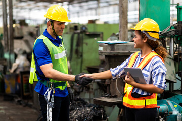 Man and Woman engineering wearing safety goggles and hard hats giving high five and celebrating success. Metal lathe industrial manufacturing factory