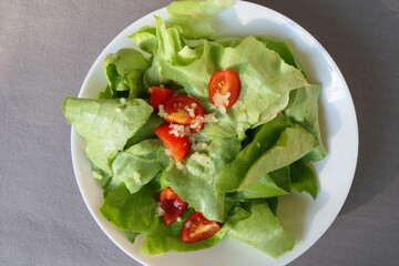 Served green lettuce with sliced mini tomatoes and fresh garlic, in white plate, from above