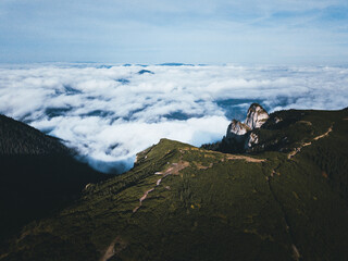 Aerial drone view of Ceahlau Massif with mist and low clouds covering the forest.