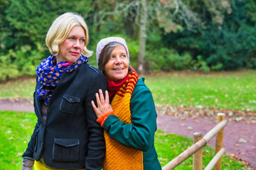 two women in their 50s hugging each other in park in autumn