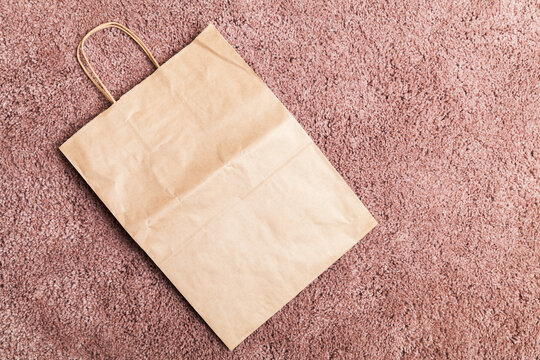 An empty flat paper bag lays on pink carpet