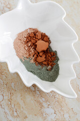 Green, red and pink bentonite clay powder in a white porcelain bowl. Clay texture close up....