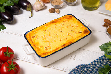 Greek Moussaka close up in casserole dish with the ingredients on the white rustic table.