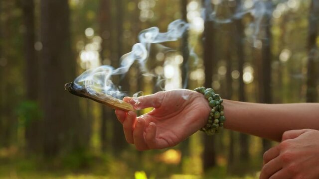 occult science and supernatural concept - young woman or witch with smoking palo santo stick performing magic ritual in forest