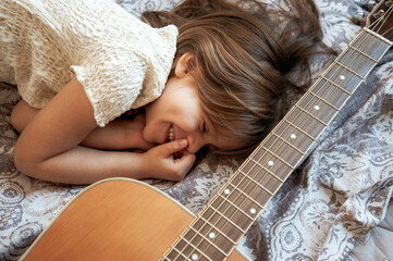 Little dreamer girl lying with her acoustic guitar - Cute female child with closed eyes smiling...