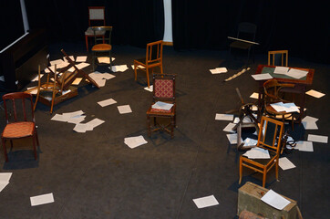 Old-fashioned chairs, chests and pieces of paper put in a mess on a theatre stage