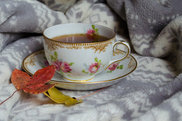 Cup of tea with flowers, vintage china, with cosy grey plaid and autumn leaves