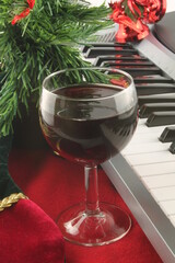 Glass of red wine with piano keys and Christmas decorations in the background, in vertical format, Christmas music, elegant celebrations concept