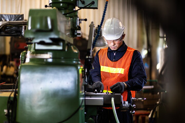 Mechanical Engineering control lathe machine in factory facility. Safety First at work place. Man Worker at industrial factory wearing uniform and hardhats.