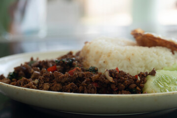 Beside view Rice topped with stir-fried beef and basil in the white plate. Blurred background is tile black color.