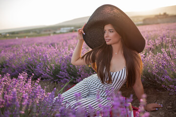 Pretty girl is wearing big hat sitting in lavender field, France.