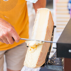 Raclette chauffée sur un four suisse et raclée avec un couteau par un homme avant dégustation