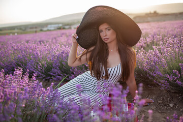 Pretty girl is wearing big hat sitting in lavender field, France.