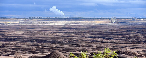 Abraumlandschaft des Braunkohle-Tagebaus in Welzow mit rauchenden Schornsteinen am Horizont