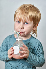 A child drinks juice from a bottle through a straw and looks at the camera