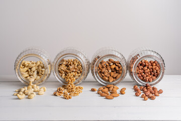 Cashew, Mandel, Walnuss und Haselnuss in liegenden Gläsern auf weißem Holztisch