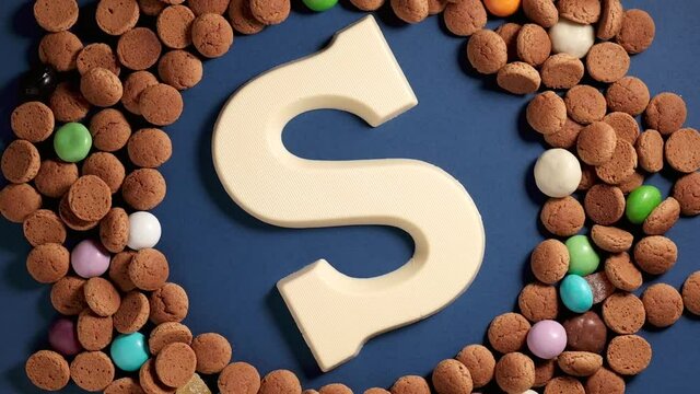 Rotation of kruidnoten, traditional sweets, strooigoed and white chocolate letter S. Background for Dutch holiday Sinterklaas. St. Nicholas day concept. FullHD video, top view