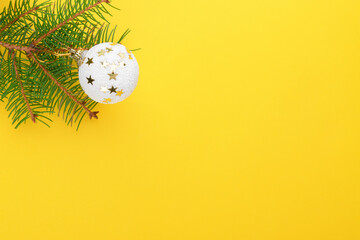 Christmas background, natural fir tree branches with white christmas balls and pines on yellow background