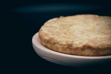tortilla de patata con huevos, patatas y cebolla sobre fondo negro. 