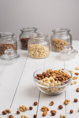 Cashew, Mandel, Walnuss und Haselnuss in Glasschüssel mit Vorrat im Hintergrund auf weißem Holz