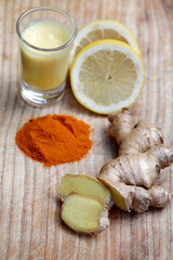 Ginger drink or shot with healthy ingredients super foods like ginger root, lemon, turmeric, wooden background, top view.