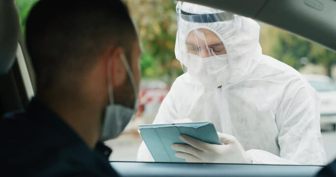 An young man is getting tested at a coronavirus by nasopharyngeal swab by medical staff with PPE suit at drive thru station.