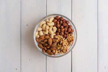 Cashew, Mandel, Walnuss und Haselnuss in Glasschüssel rechts oben auf weißem Holz
