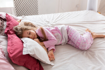 A little girl in pink pajamas is fast asleep on a comfortable bed