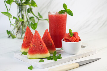 Buah Semangka or watermelon fruit, cut on wooden white chopping board, with a bowl of slices watermelon and watermelon juice. Bright mood photo on white marble background.