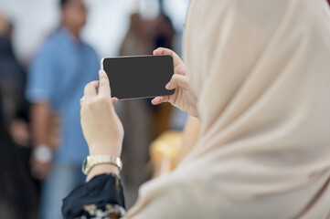 Muslim girl Wearing a cream-colored hijab, using a smartphone take pictures of current events to deliver news to your colleagues in the office. Social change that made everything very fast.