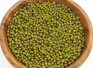 On a white background in a wooden round plate lie oval green beans for sprouting
