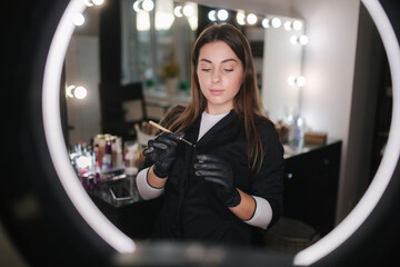 Portrait of professional female brow master in black robe with black gloves use brush and henna for...