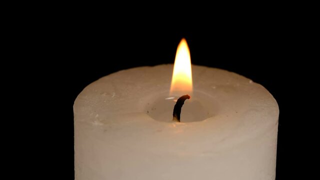 Large thick white candle lit and burn on a black background high resolution video clip macro shooting close-up