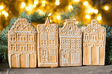Christmas cookies gingerbread houses on wooden table with christmas lights in background, selective focus.