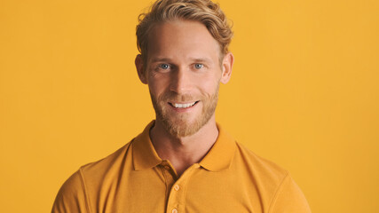 Handsome positive bearded man happily looking in camera and smiling isolated on yellow background