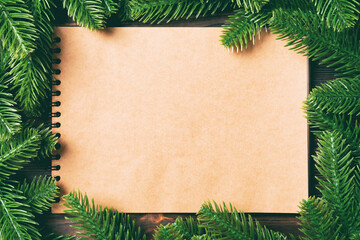 Top view of notebook made of craft paper decorated with a frame made of fir tree on wooden background. New Year time concept
