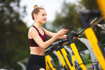 Naklejka premium Young woman in sportswear scans qr code with her phone to rent yellow electric scooter.