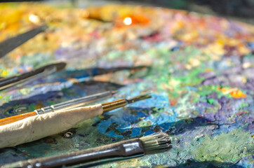 Stock Photo of a painter brushes and palette knife on a wooden palette with mixed and unmixed oil colours on sunlight. Concept art painter