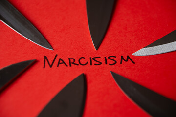 Word Narcisism, written in black on red paper, with knife blades next to it.