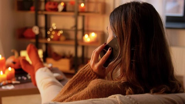people, holidays and leisure concept - young woman calling on smartphone at home on halloween