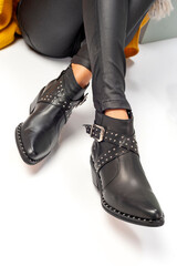 
legs of a woman wearing a collection of fashionable leather shoes on a set with cubes and gray walls and a white floor